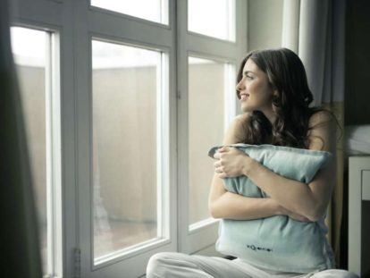 a woman sitting on a window sill holding a pillow